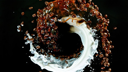 Fresh roasted coffee beans with milk splash flying in the air in vortex shape, isolated on black...