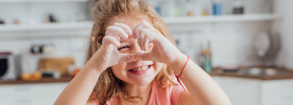 horizontal image of girl showing heart sing with hands in flour in kitchen