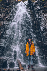 woman in yellow raincoat at autumn waterfall