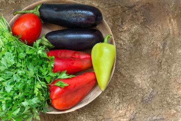 Red tomato, pepper, parsley, eggplant lie on a wooden plate on a brown background. view from above. Copy space