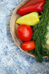 Red tomatoes, yellow-green and red peppers, dill, cabbage lie on a wooden plate on a blue background. view from above. Copy space