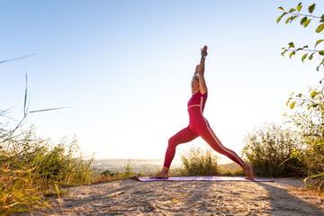 Girl with light short hair standing and pulling her hands up while training yoga poses by the sea