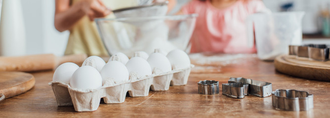 selective focus of chicken eggs and cookie cutters near woman and child sieving flour, horizontal concept
