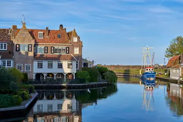 Deurstickers Malerische Ansicht mit Wasserspiegelungen und alten historischen Gebäuden in Enkhuizen am Ijsselmeer in den Niederlanden, mit Blick auf den Kanal zum Hafen Oosterhaven in dem ein Fischerboot liegt. © Lichtfreibeuter