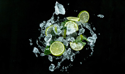 Fototapeta na wymiar Fresh ripe limes with ice cubes flying on a black background. Freeze motion.