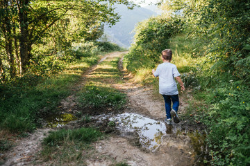 Naklejka na ściany i meble 6-year-old boy jumps a puddle in the woods
