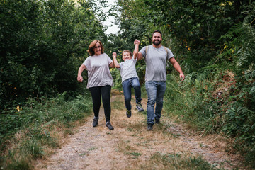 family of father, mother and 6-year-old walks in the woods. The child jumps with the help of his parents and everyone smiles