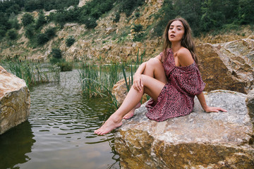 young  beautiful brunette woman sitting on a lake in a forest 