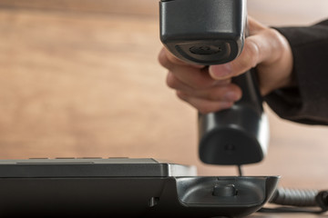 Businessman hand picking or hanging up a black landline telephone handset