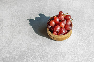 A bunch of red grapes on a light table with a hard shadow from sunlight with copy space