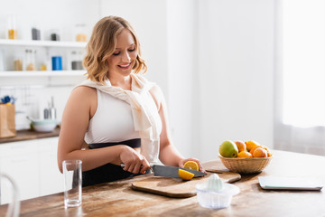 Obraz na płótnie Canvas selective focus of woman cutting lemon near laptop and fruits