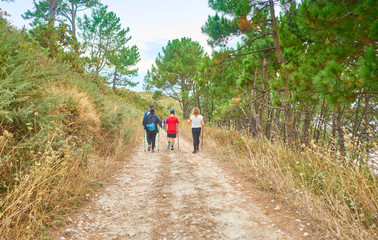 Family walking with backpacks and walking sticks along a path in the field full of trees