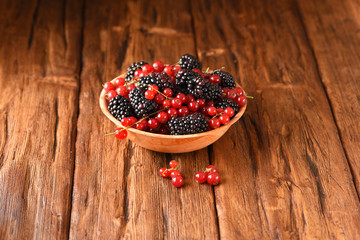 Blackberries and red currants in a wooden plate on the wooden table.
