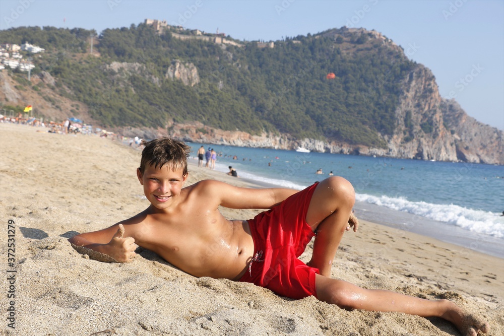 Wall mural Boy on the beach in shorts at sea in summer is played with sand