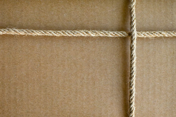 Craft paper box tied with jute rope criss-cross. Close-up. Brown textured background with rope frame. Gift close-up. grainy texture of cardboard box background.