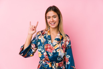 Young caucasian woman wearing pajamas showing a horns gesture as a revolution concept.
