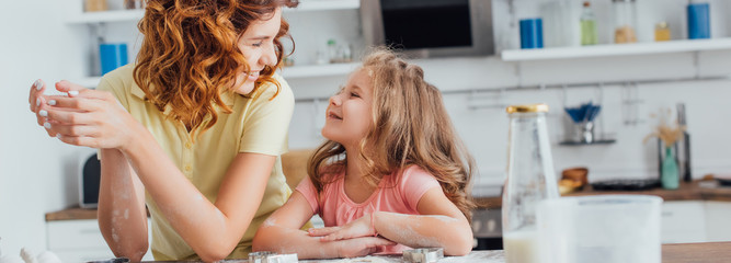 selective focus of mom and daughter looking at each other while cooking in kitchen