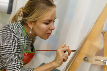 A beautiful blonde girl artist paints a picture on a canvas with oil paints