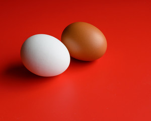 White and brown egg on a red background. Two eggs of different colors. Two raw eggs. Concept: different. Free space for text.

