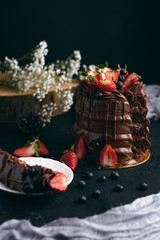  Ponqué húmedo de chocolate, relleno de fresas con crema, decorado con brigadeiro de chocolate y ganache de chocolate y arándanos con una rebanada en un plato pequeño