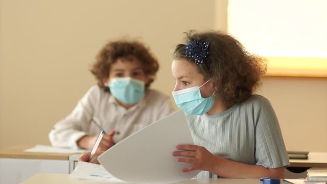 Disobedient masked students talk during the lesson. Strict teacher takes the cheat sheet and tears it