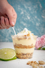 mano sacando una cucharada de un postre de limon con galletas sobre una base blanca con rodajas de limon partido y una flor