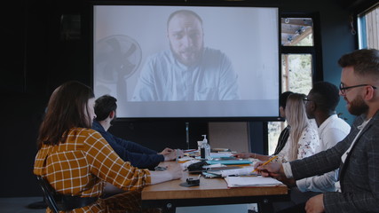 Team of diverse business people use projector for online web conference call with male boss coach at modern office.