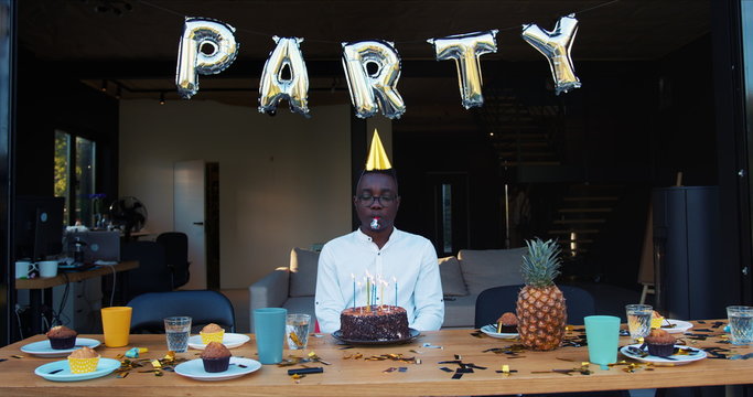 Self-isolation Ruined Birthday Party. Sad Upset African Young Man Sits Alone With Cake At Celebration Table Slow Motion.