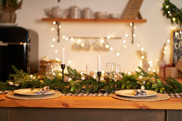 The festive Christmas table is decorated with branches of a Christmas tree, candles and garlands....