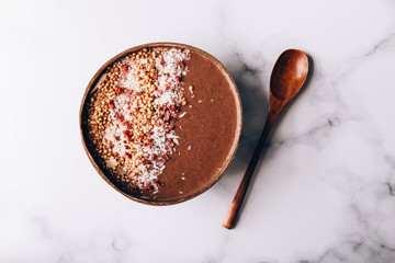 Chocolate Smoothie from Banana and Strawberries with cacao, Granola and Coconut Shreds on top in Coconut Shell Bowl, strong shadows. Healthy summer breakfast, top view