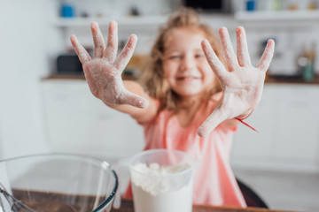 selective focus of girl showing hands in flour near measuring jug and glass bowl, panoramic shot