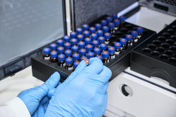 Chemist putting vial with a sample into autosampler of HPLC system. High performance liquid...