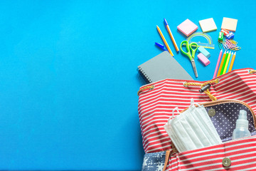 Stripped backpack with school supplies and COVID 19 prevention items. Top view, spilling onto a blue background.