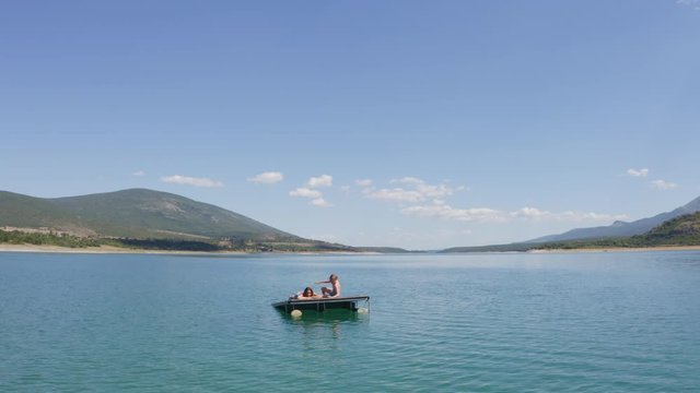 4K Mother and son have a relax on the mountain lake. They suntanning on floating platform. Flying drone aerial footage over Peruca Lake, Dalmatia, Croatia