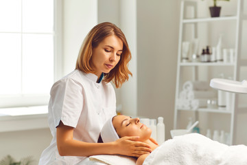 Woman cosmetologist making face massage for woman client in beauty spa salon