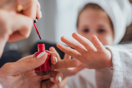 cropped view of woman applying red enamel on fingernails of daughter, selective focus