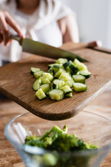 cropped view of woman holding cutting board with sliced cucumber near bowl with fresh broccoli