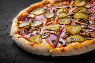 Pizza with Mozzarella cheese, ham, tomato sauce, pepper, pickled cucumbers and mushrooms. Italian pizza on Dark grey black slate background