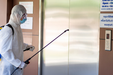 health care social worker in protective white jumpsuit with glasses and surgical face mask using spraying machine to disinfect corona virus pandemic in the office 