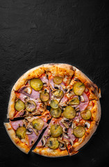 Pizza with Mozzarella cheese, ham, tomato sauce, pepper, pickled cucumbers and mushrooms. Italian pizza on Dark grey black slate background