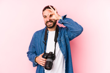 Young caucasian photographer man isolated excited keeping ok gesture on eye.