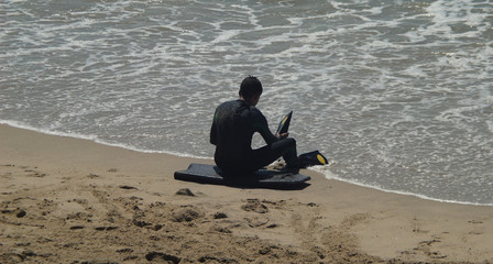 Adolescente com fato de neoprene vestido sentado numa prancha de bodyboard a calçar uma barbatana