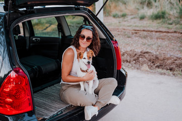 Fototapeta na wymiar young happy woman in a car enjoying with her cute dog. Travel concept