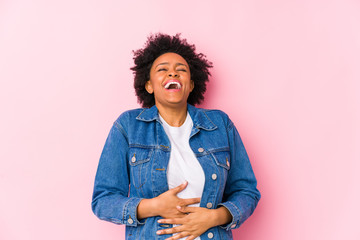 Young african american woman against a pink backgroound isolated laughs happily and has fun keeping...