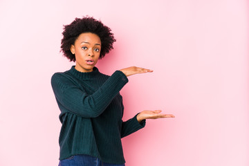 Middle aged african american woman against a pink background isolated shocked and amazed holding a copy space between hands.