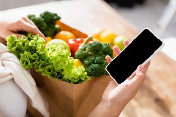 selective focus of woman holding smartphone with blank screen near groceries