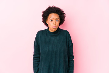 Fototapeta na wymiar Middle aged african american woman against a pink background isolated shrugs shoulders and open eyes confused.