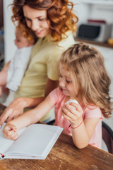 selective focus of mother pointing with finger at cookbook while daughter holding chicken egg