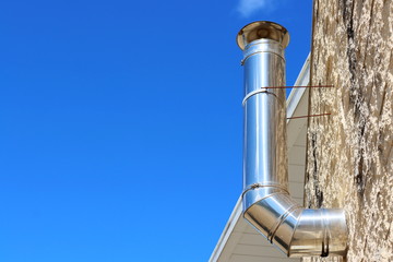 A stainless steel ventilation pipe for supplying and exhausting air and gas from a gas boiler on the top floor of a house against a blue sky. Concept: preparing the heating system for the cold season.