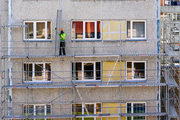 the worker assembles the scaffolding on the facade of a multi-storey house at a dangerous height